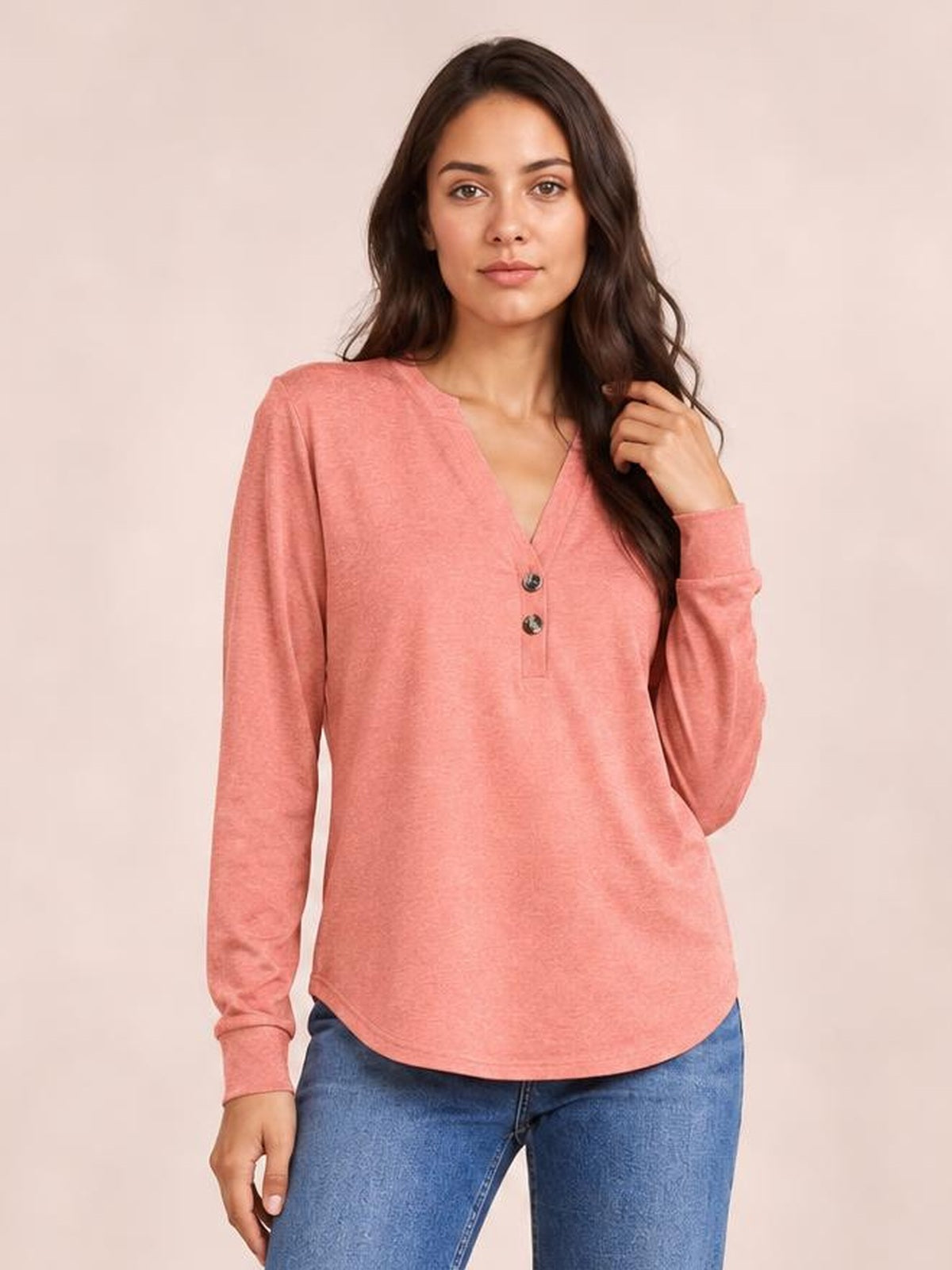 Model wears a coral pink long sleeve top with a notched V-neck, two-button placket, relaxed straight silhouette, and curved hem.