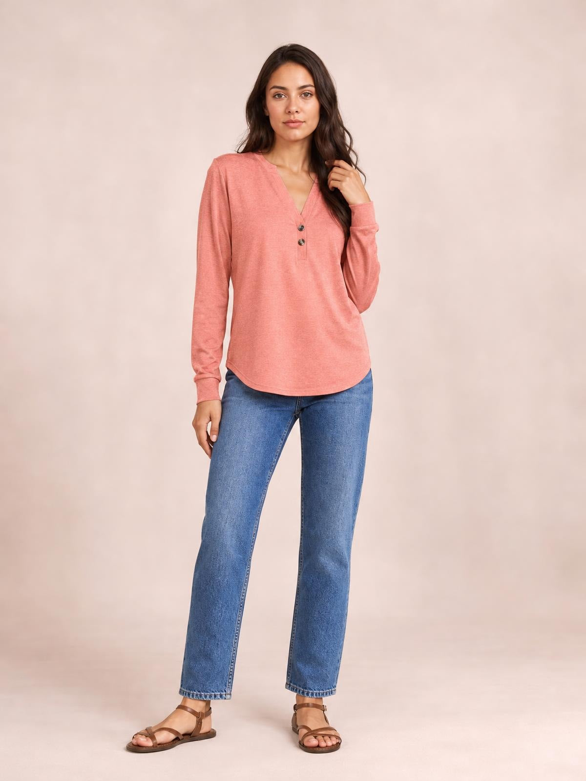 Model poses in a coral long sleeve top with a notched neckline, two-button placket, relaxed straight silhouette, and rounded hem.