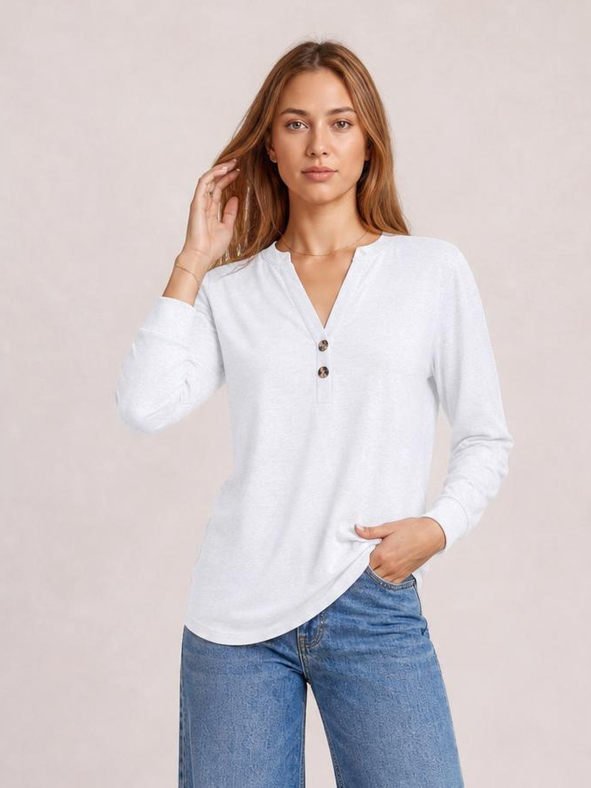 A model poses in a white long-sleeve top with a notched neckline, two-button front, relaxed silhouette, and gently curved hem.