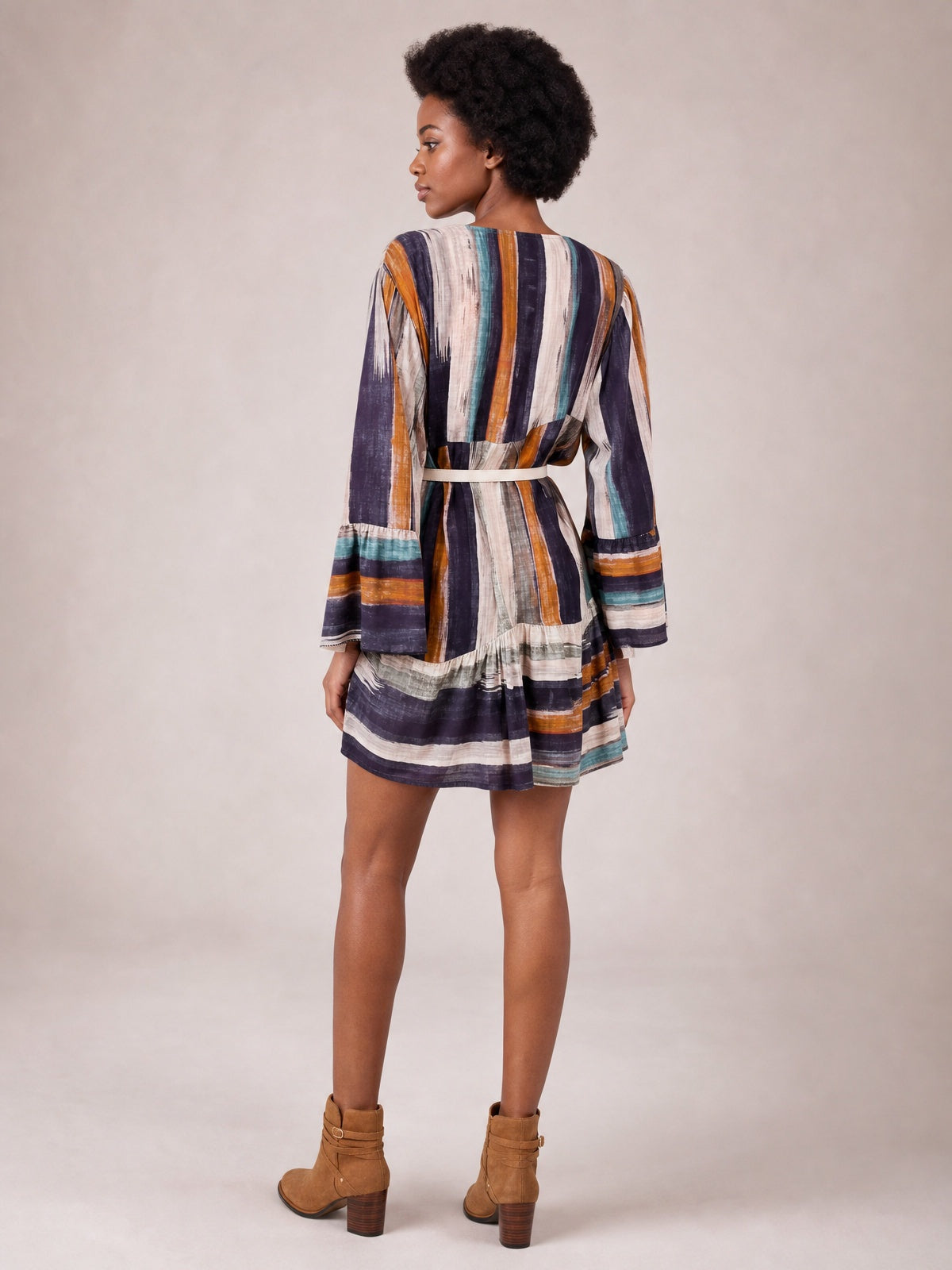 A model poses turned away in a multicolored striped buttoned mini dress with long sleeves, a defined waist, and softly flared skirt.