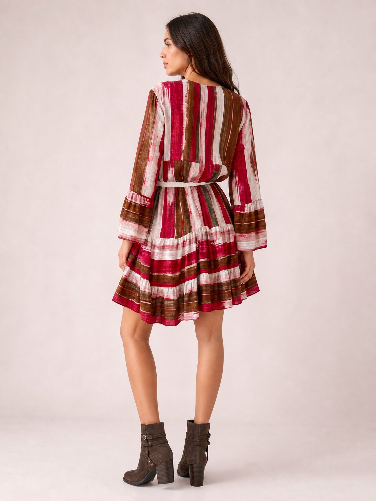 Back view of a model wearing a burgundy, brown, and white striped long-sleeve mini dress with a defined waist and tiered, flared skirt.