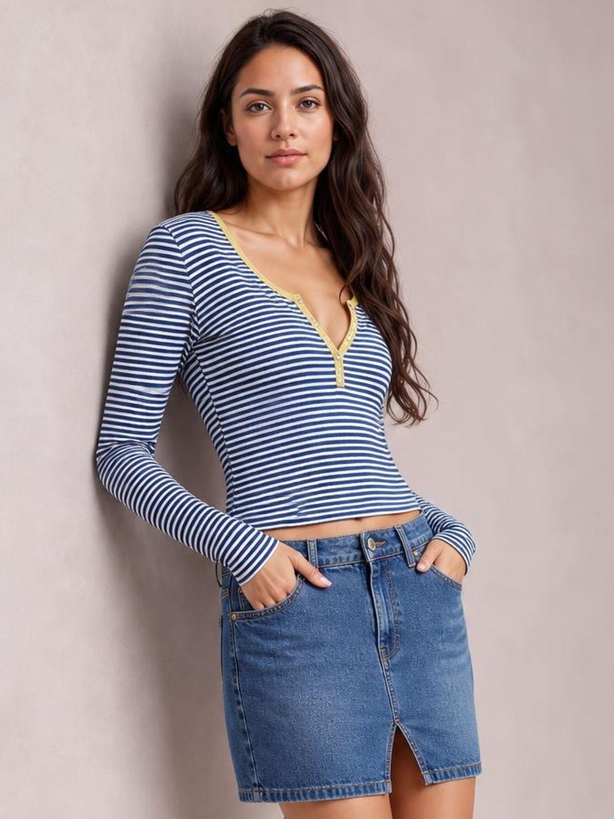 Model wearing a fitted navy-and-white striped long sleeve T-shirt with a buttoned V-neck placket, leaning with hands in jean pockets.
