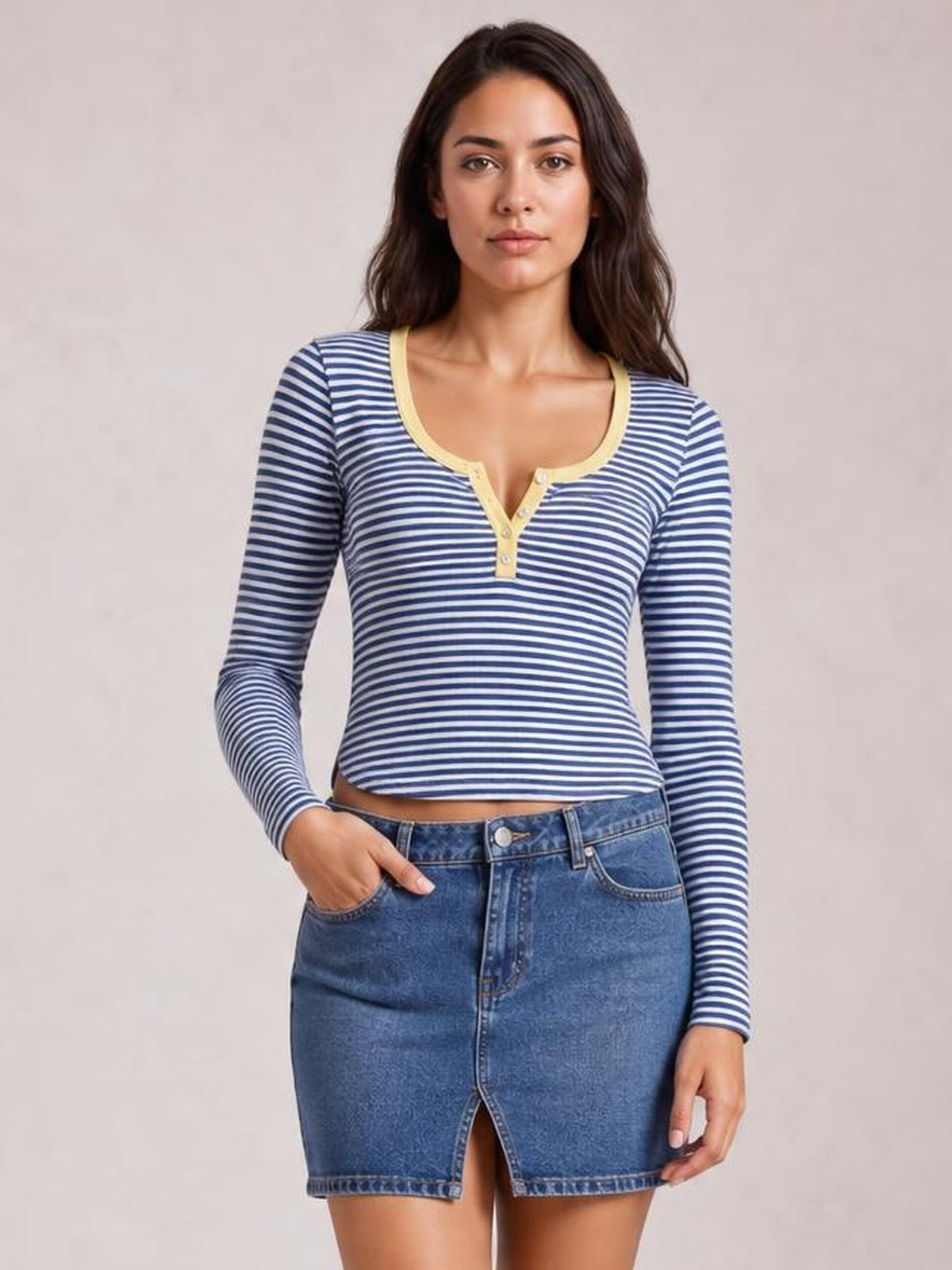 Model wearing a navy and white striped long sleeve T-shirt with a buttoned scoop neckline, fitted cropped silhouette, and one hand in a denim skirt pocket.