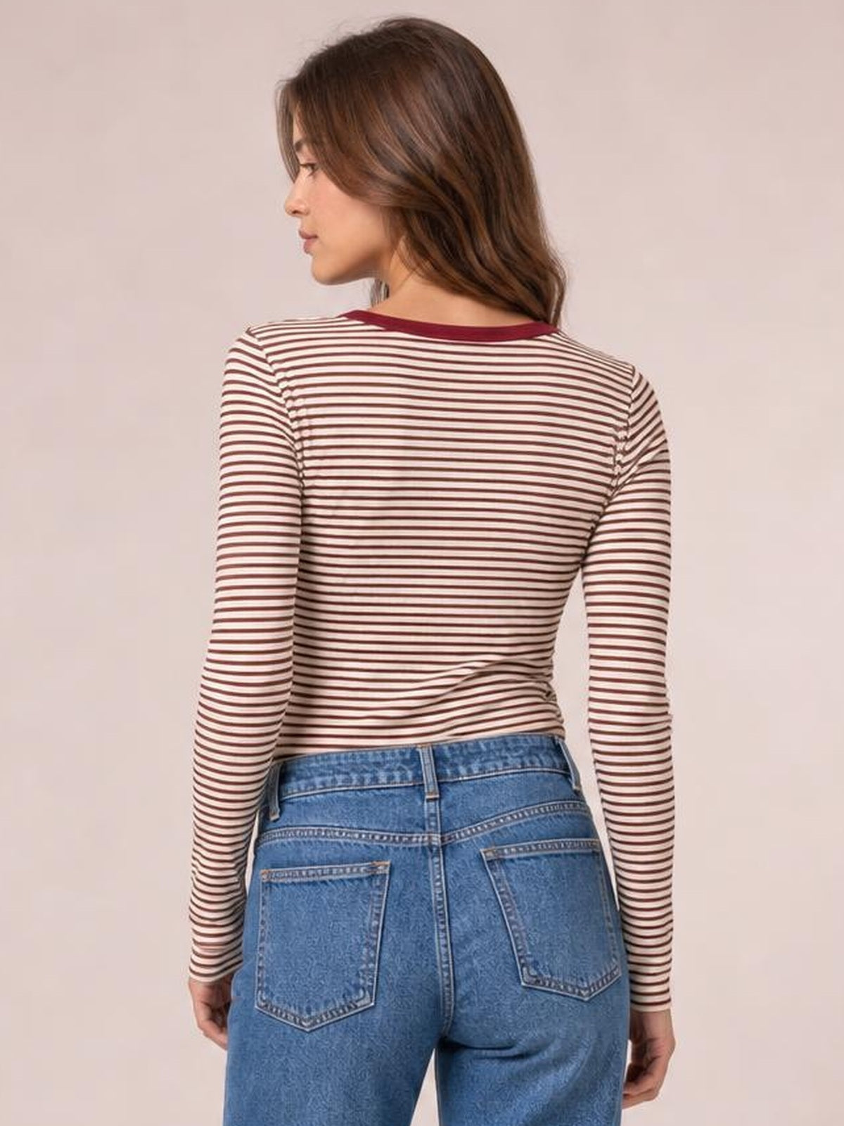 Model shown from behind in a fitted cream-and-burgundy striped long sleeve T-shirt, turning slightly to reveal its rounded neckline and smooth silhouette.