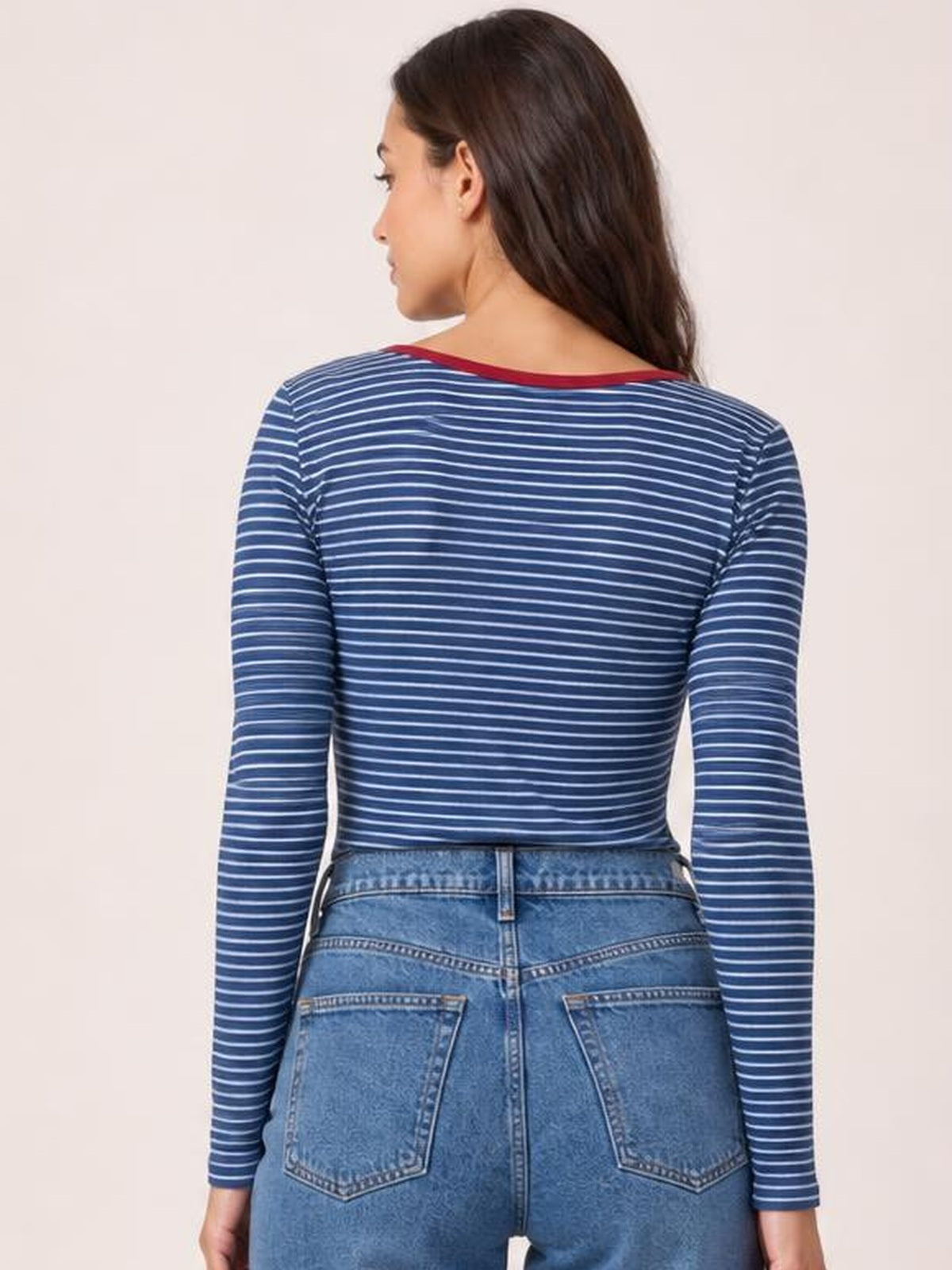 A model turned away wears a navy-and-white striped long-sleeve T-shirt with a fitted, waist-length silhouette and contrasting red neckline trim.