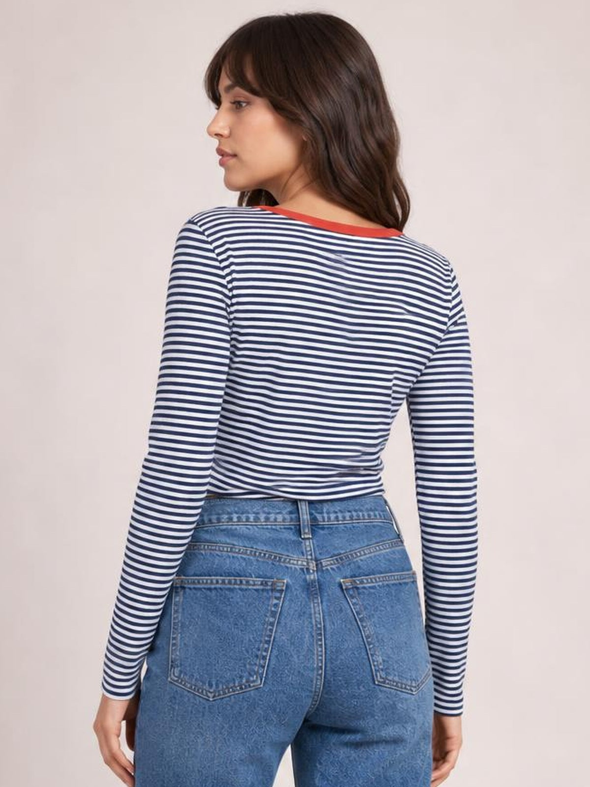 Model turned away wears a navy and white striped long sleeve T-shirt with a relaxed silhouette, button detailing near the shoulder, and a contrasting neckline.