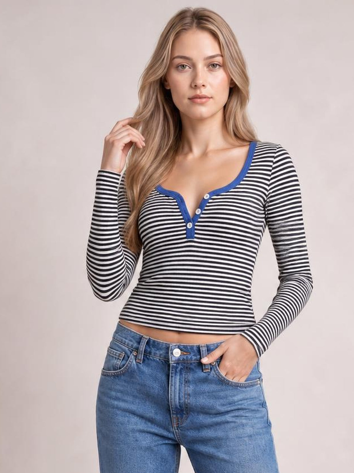 Model poses with one hand in her pocket wearing a fitted black-and-white striped long sleeve T-shirt with a blue-trimmed buttoned neckline and waist-length silhouette.