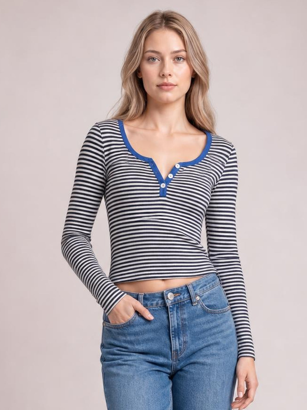 Model wearing a fitted black-and-white striped long sleeve T-shirt with blue trim and a buttoned scoop neckline, posing with one hand in her jeans pocket.