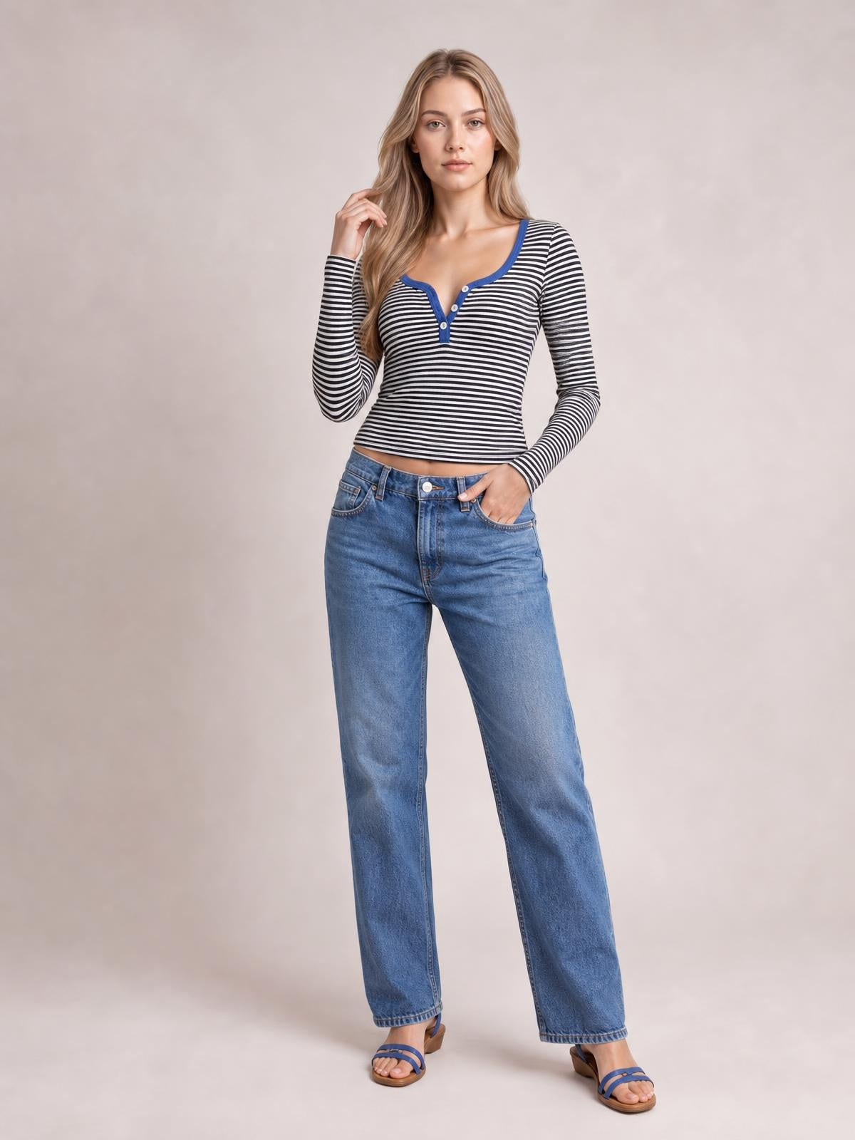 Model wearing a fitted black-and-white striped long sleeve T-shirt with a blue-trimmed button placket, paired with relaxed blue jeans.