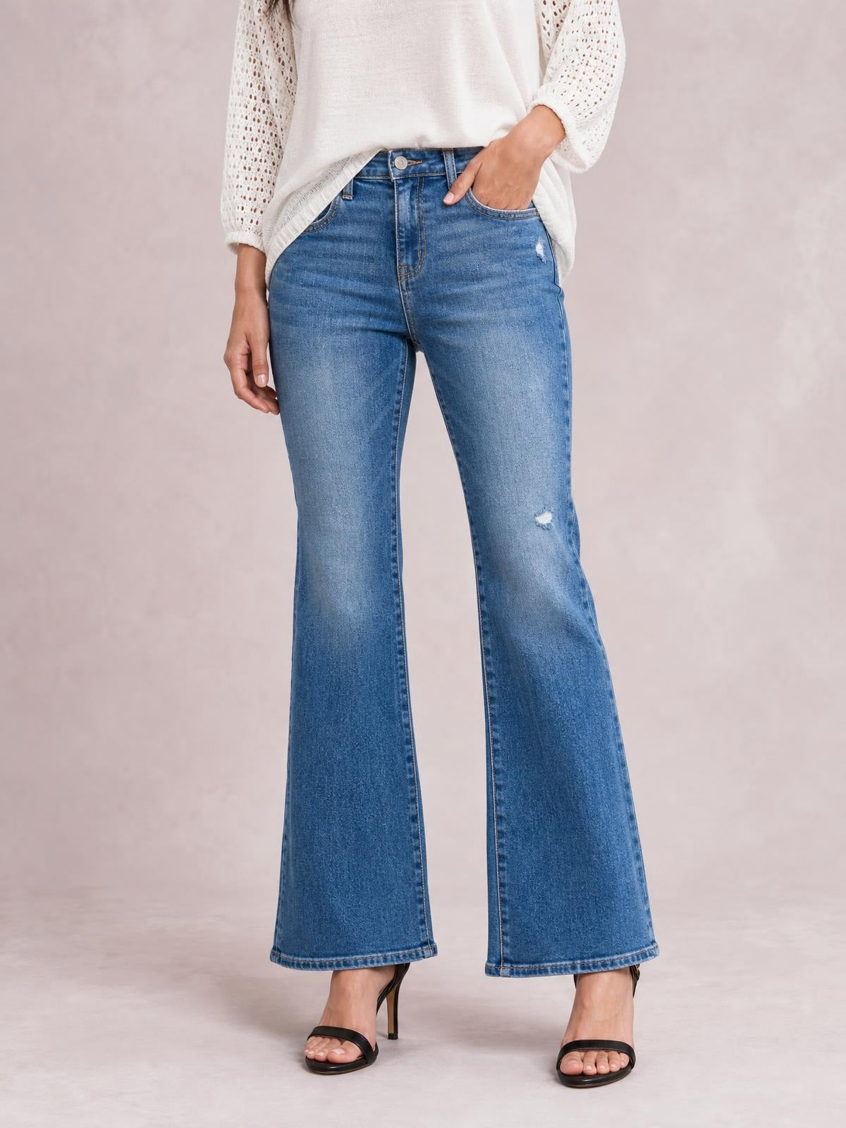 Model wearing blue high-rise bootcut jeans with front pockets, distressed details, a fitted waist and thighs, and flared hems.