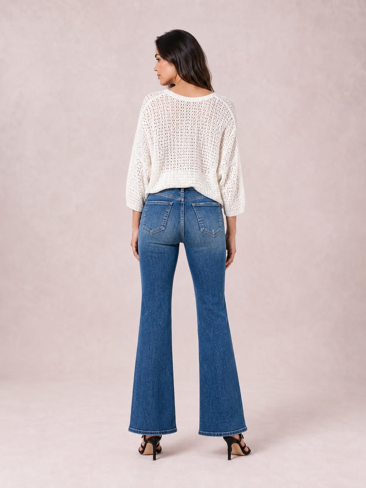 Model shown from behind wearing blue high-rise bootcut jeans with back pockets, a fitted seat, subtle distressed finish, and flared leg openings.