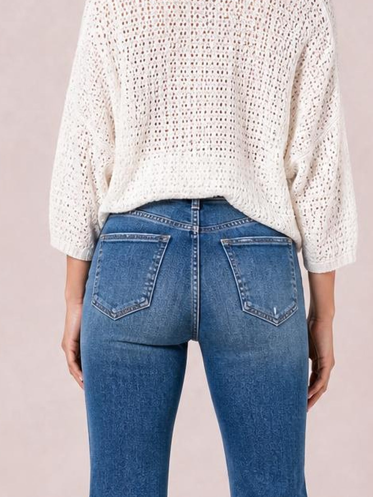 A model stands from the back wearing blue high-rise bootcut jeans with a fitted silhouette, belt loops, contrast stitching, and two functional back pockets.