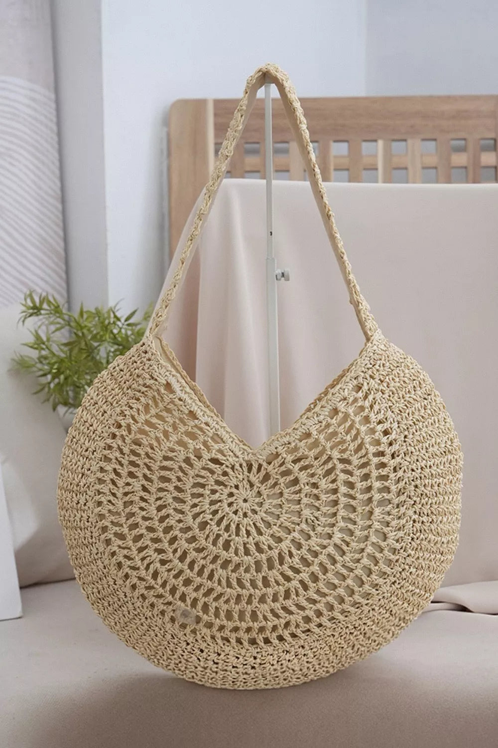 Medium beige round woven shoulder bag with an open crochet design, circular floral motif, sturdy braided strap, and softly curved silhouette.