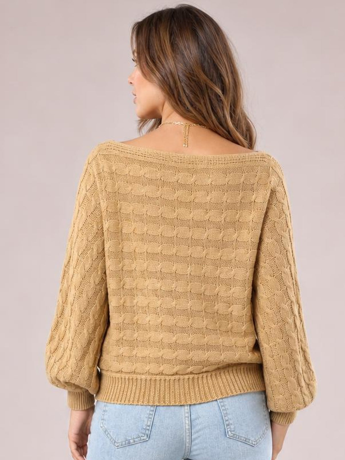 Model shown from the back wearing a camel cable-knit boat neck sweater with long sleeves, ribbed cuffs and hem, and a relaxed silhouette.