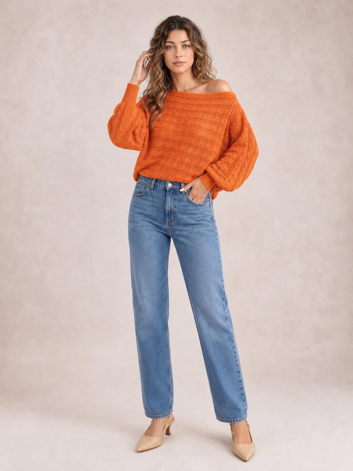 Model wearing an orange cable-knit boat neck sweater with a relaxed silhouette, balloon sleeves, ribbed cuffs, and one shoulder exposed.