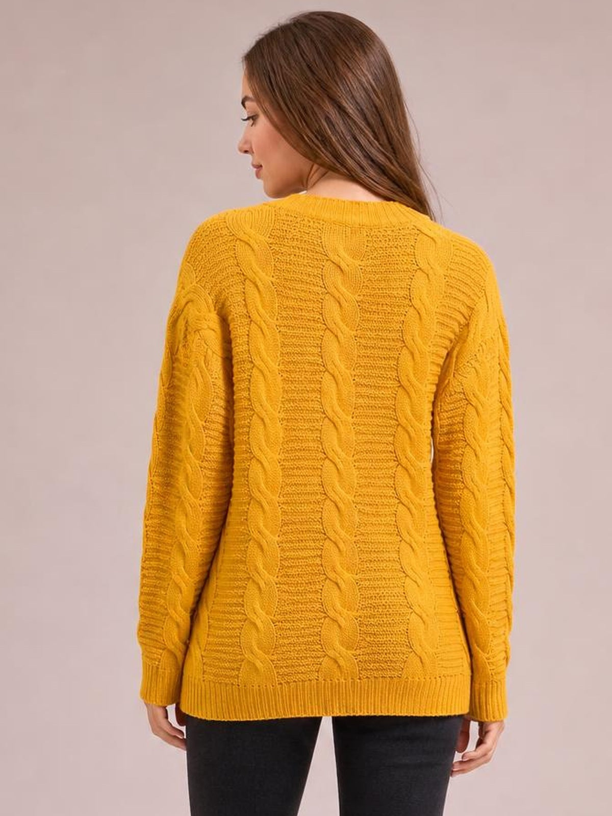 A model shows the back of a mustard yellow cable-knit long-sleeve cardigan with a relaxed silhouette, vertical braided texture, ribbed cuffs, neckline, and hem.