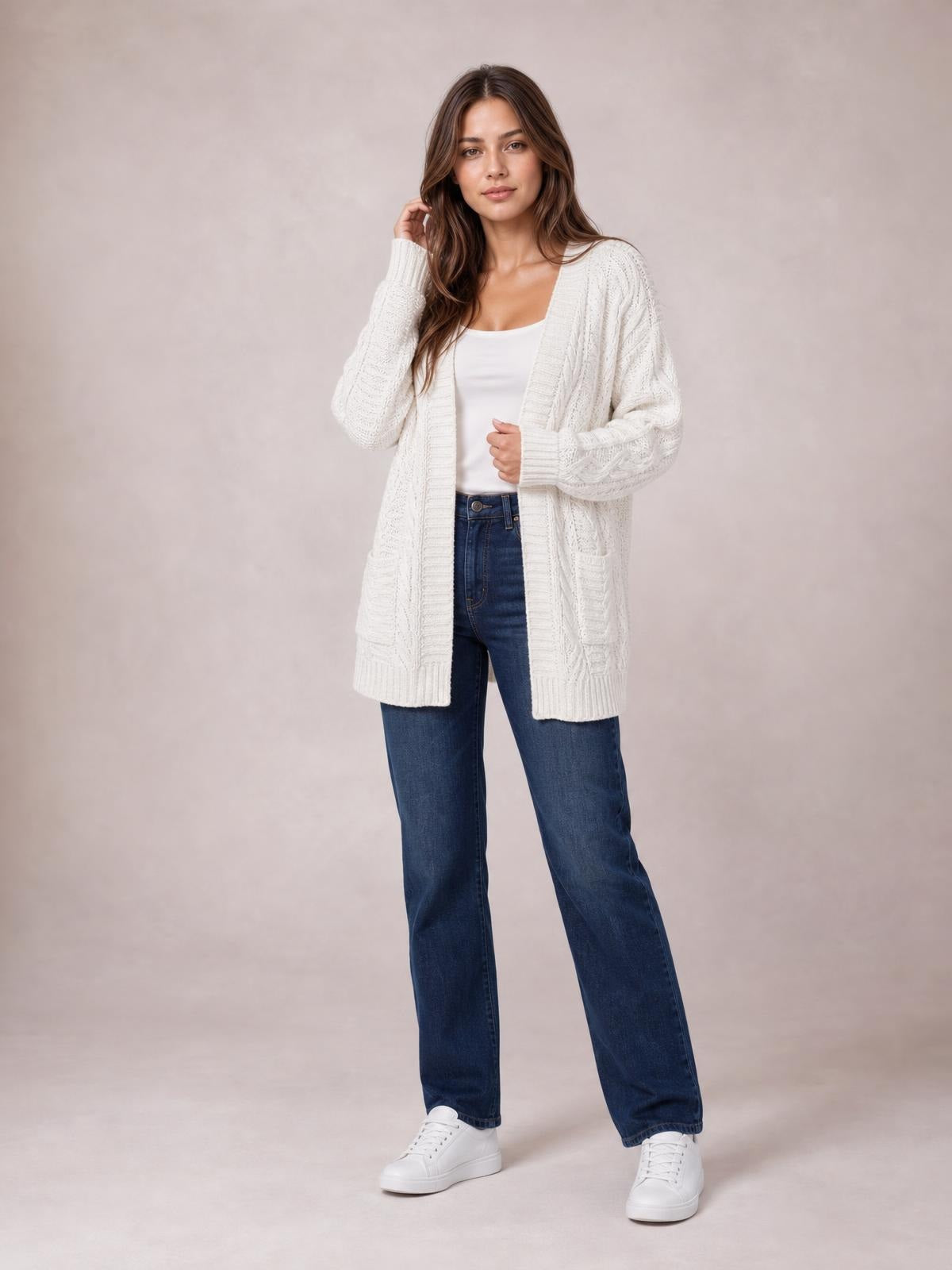 Model wearing a white cable-knit open front long sleeve cardigan with a relaxed long silhouette, ribbed edges, and textured knit panels over a tank top.