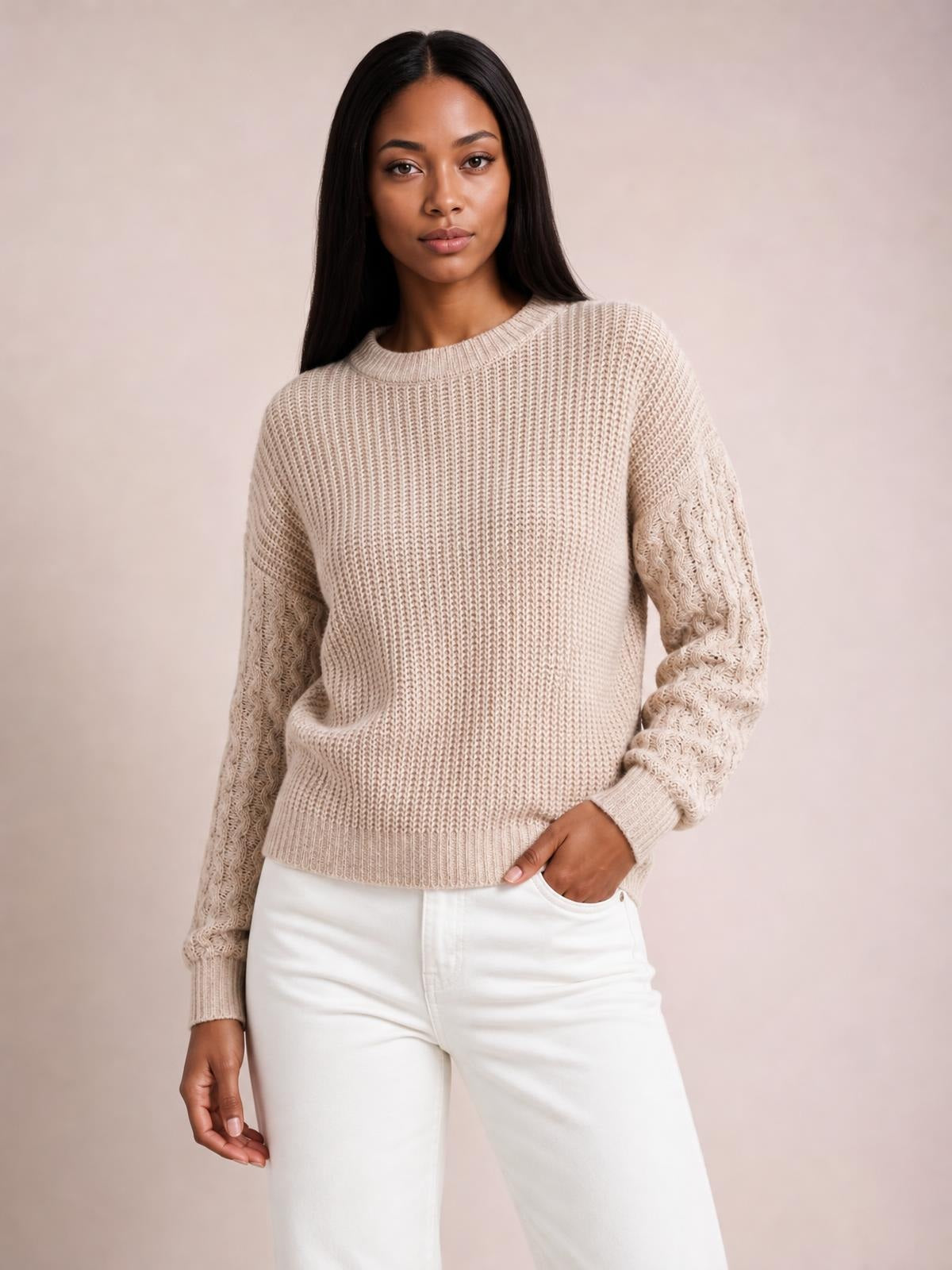 Model wears a beige cable-knit round neck sweater with dropped shoulders, textured sleeves, ribbed trims, and a relaxed silhouette, posing with one hand in her pocket.