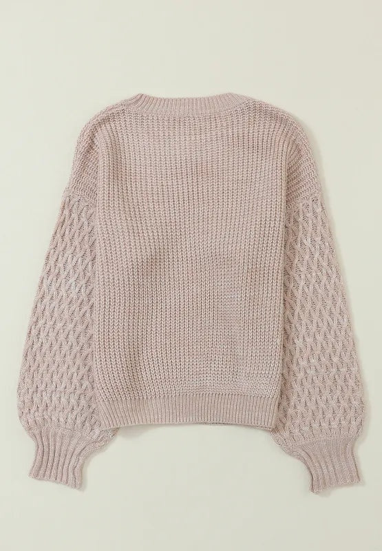 Blush pink cable-knit sweater laid flat, featuring a relaxed dropped-shoulder silhouette, ribbed round neckline, cuffs, and hem.