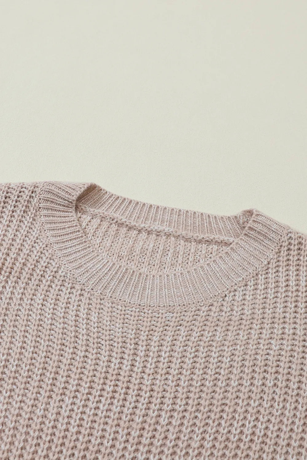 Close-up of a soft taupe cable-knit sweater showing its ribbed round neckline, textured stitch pattern, and relaxed dropped-shoulder construction.