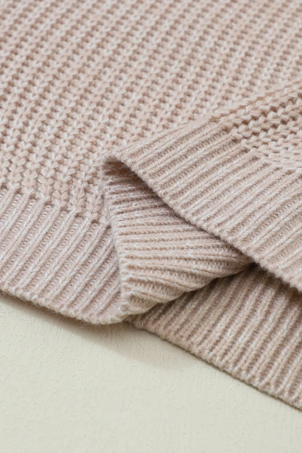 Close-up of a soft beige cable-knit sweater showing its textured construction and wide ribbed sleeve cuff.