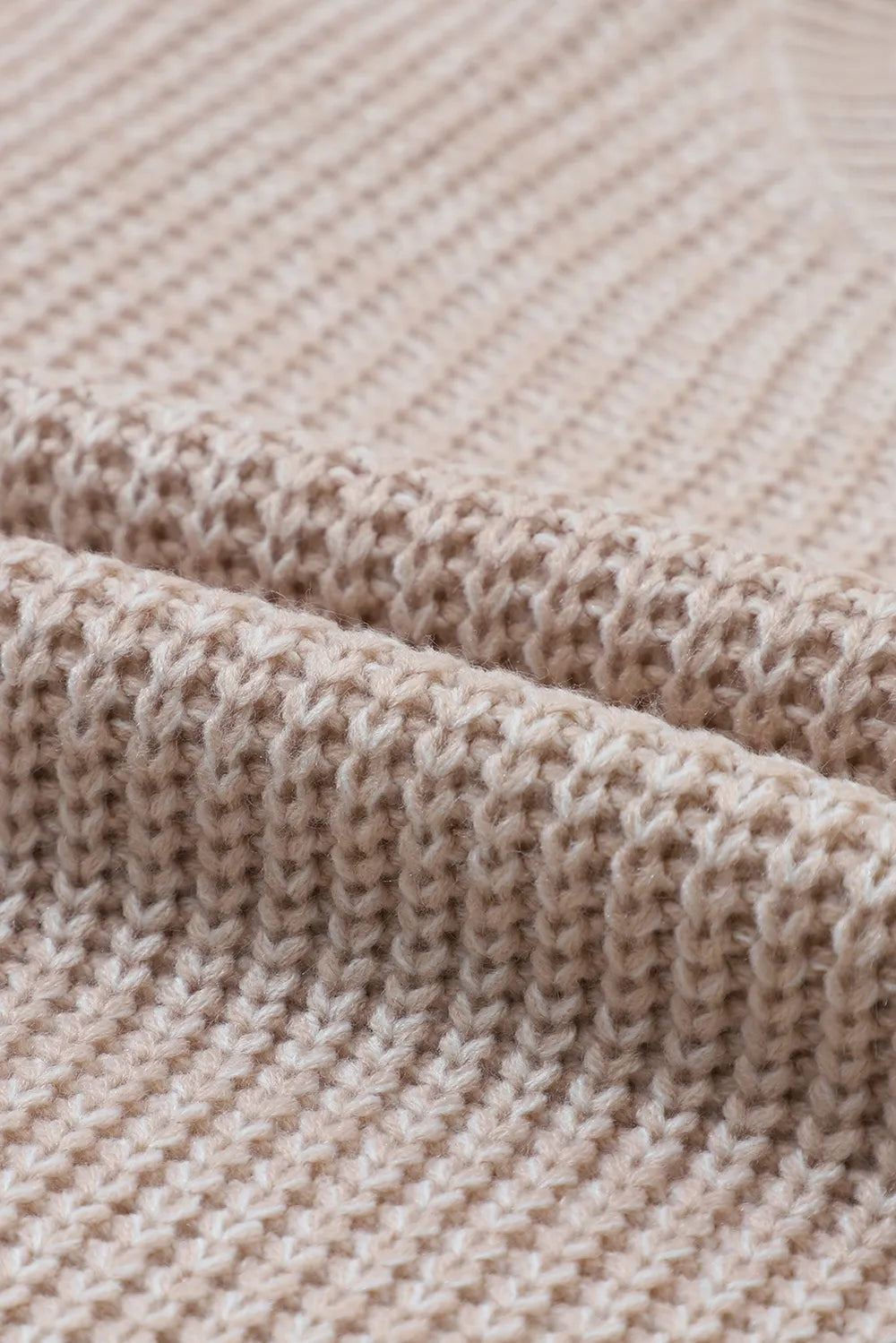 Close-up of a pale beige cable-knit sweater showcasing its chunky textured construction and soft, slightly nubby acrylic knit.