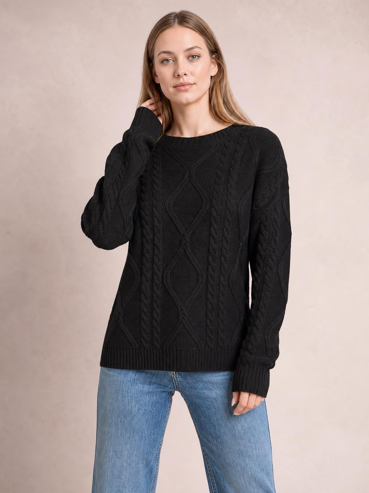 Model wearing a black cable-knit round-neck sweater with long sleeves, ribbed cuffs and hem, relaxed silhouette, posing with one hand near her neck.
