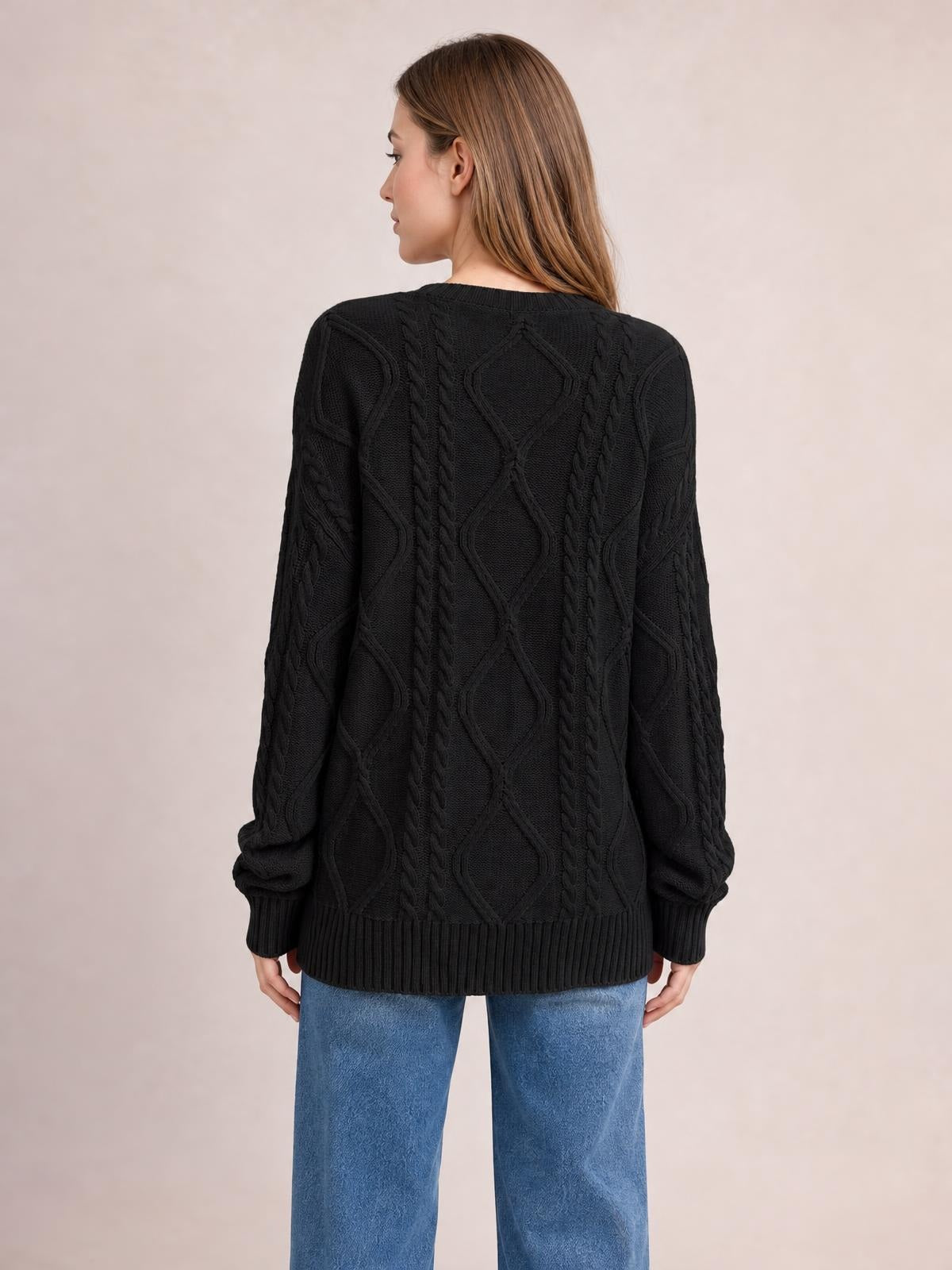 Model shown from the back wears a black cable-knit round-neck sweater with long sleeves, a relaxed silhouette, and ribbed cuffs and hem.