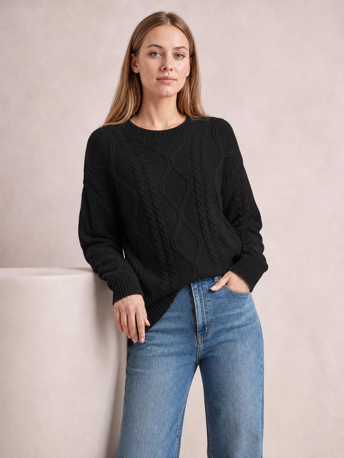 Model wears a black cable-knit round-neck sweater with long sleeves, ribbed cuffs and hem, relaxed silhouette, and textured braided panels.