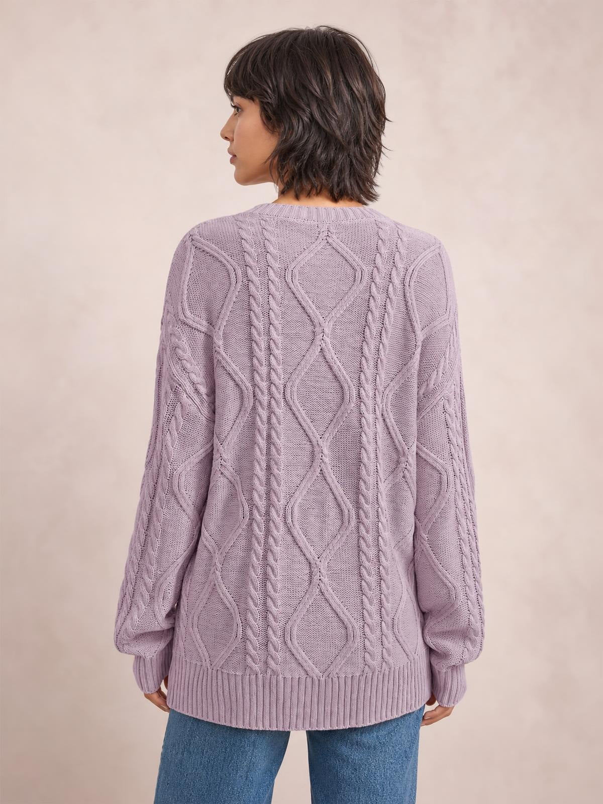 Model shown from behind wearing a lavender cable-knit round-neck sweater with long sleeves, ribbed cuffs and hem, and a relaxed silhouette.