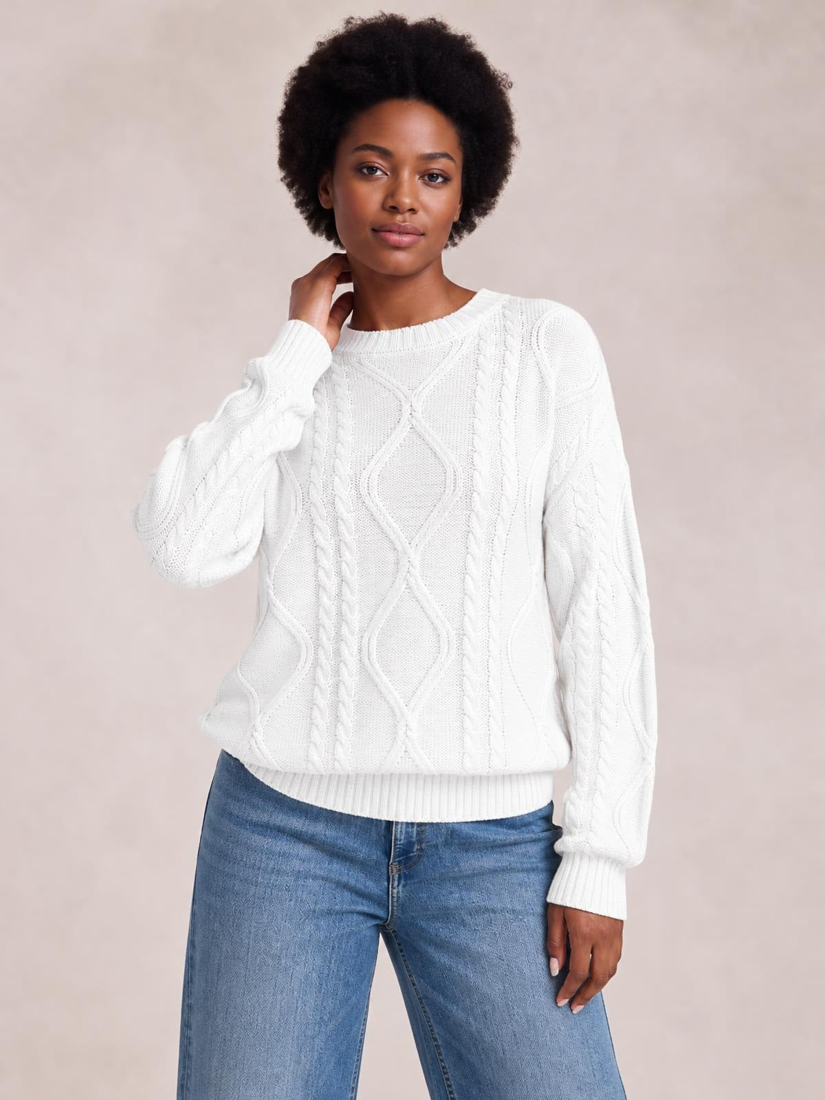 A model poses in a white cable-knit round neck sweater with long sleeves, ribbed cuffs and hem, and a relaxed straight silhouette.
