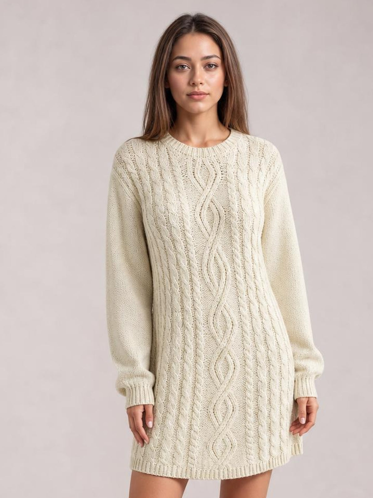 Model stands facing forward in an ivory cable-knit sweater mini dress with long sleeves, ribbed trim, seam detail, and a relaxed straight silhouette.