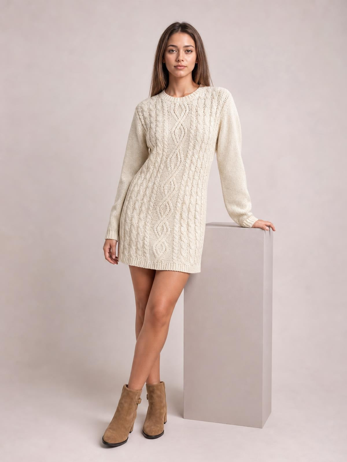 Model in a cream cable-knit sweater mini dress with long sleeves, round neckline, textured seams, straight silhouette, and crossed-leg pose.