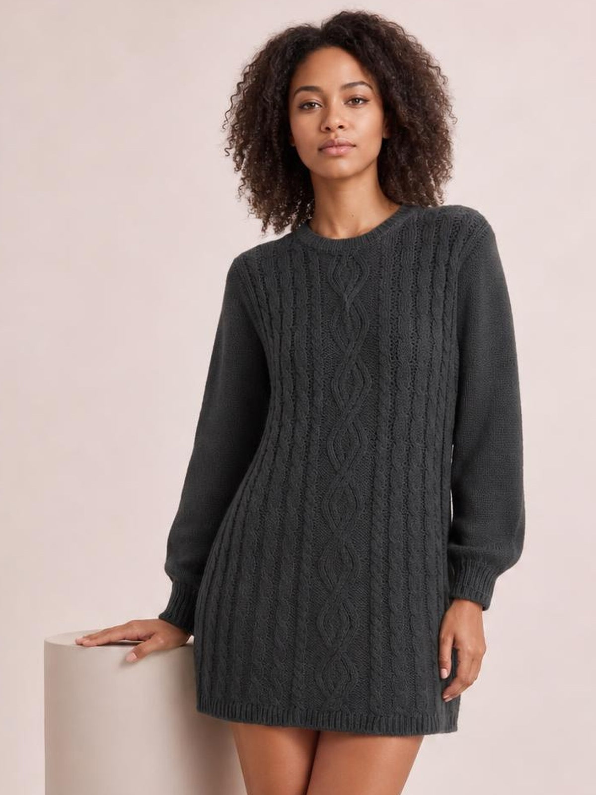 A model poses in a charcoal cable-knit sweater mini dress with a relaxed straight silhouette, crew neckline, long sleeves, ribbed cuffs, and hem.