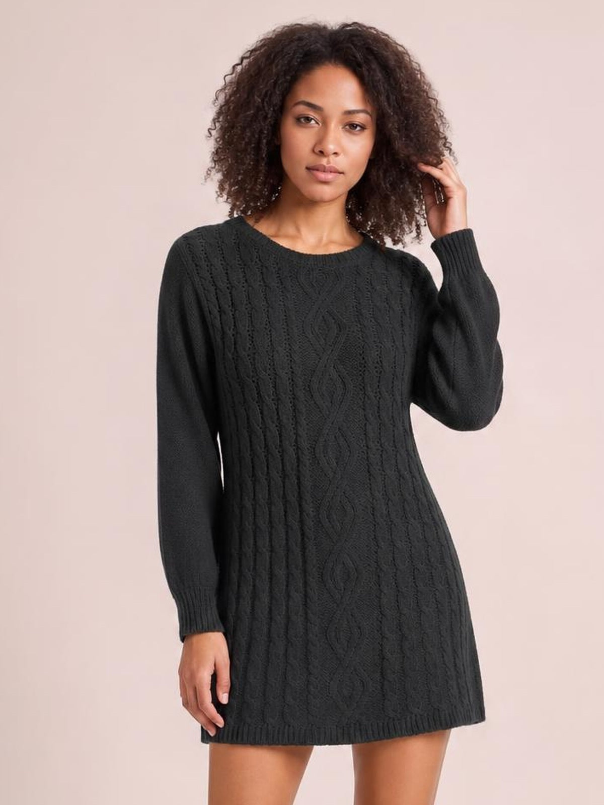Model poses in a black cable-knit sweater mini dress with long sleeves, ribbed trim, a round neckline, seam detail, and a relaxed straight silhouette.