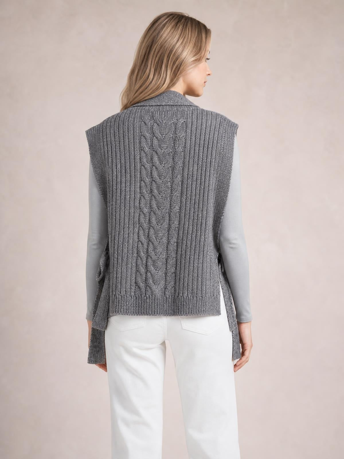 Model shown from behind wearing a gray cable knit sweater vest with a sleeveless silhouette, ribbed edges, and a central braided cable pattern.
