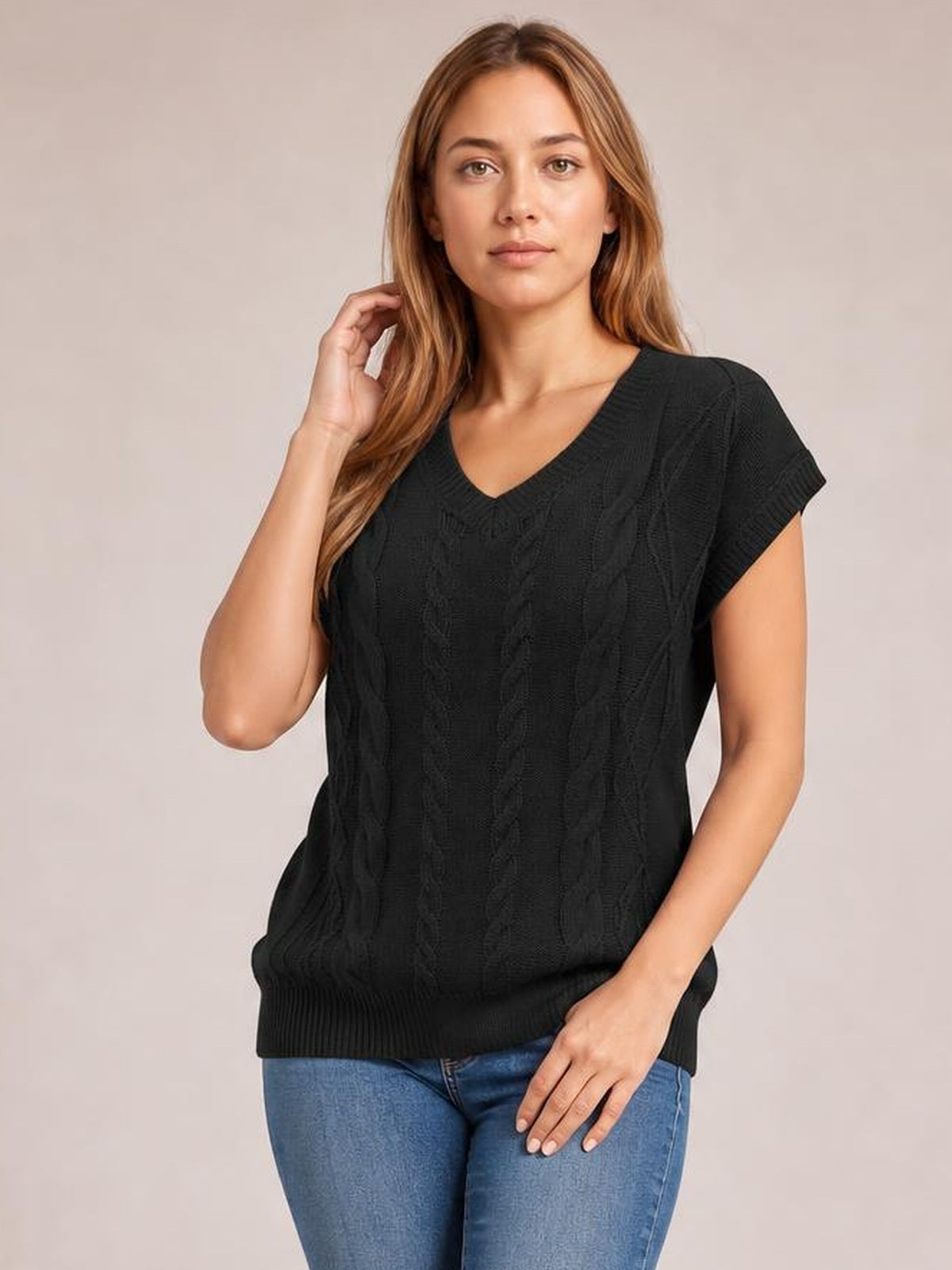 Model wearing a black cable-knit V-neck short sleeve top with a relaxed silhouette, ribbed neckline and hem, posing with one hand near her hair.