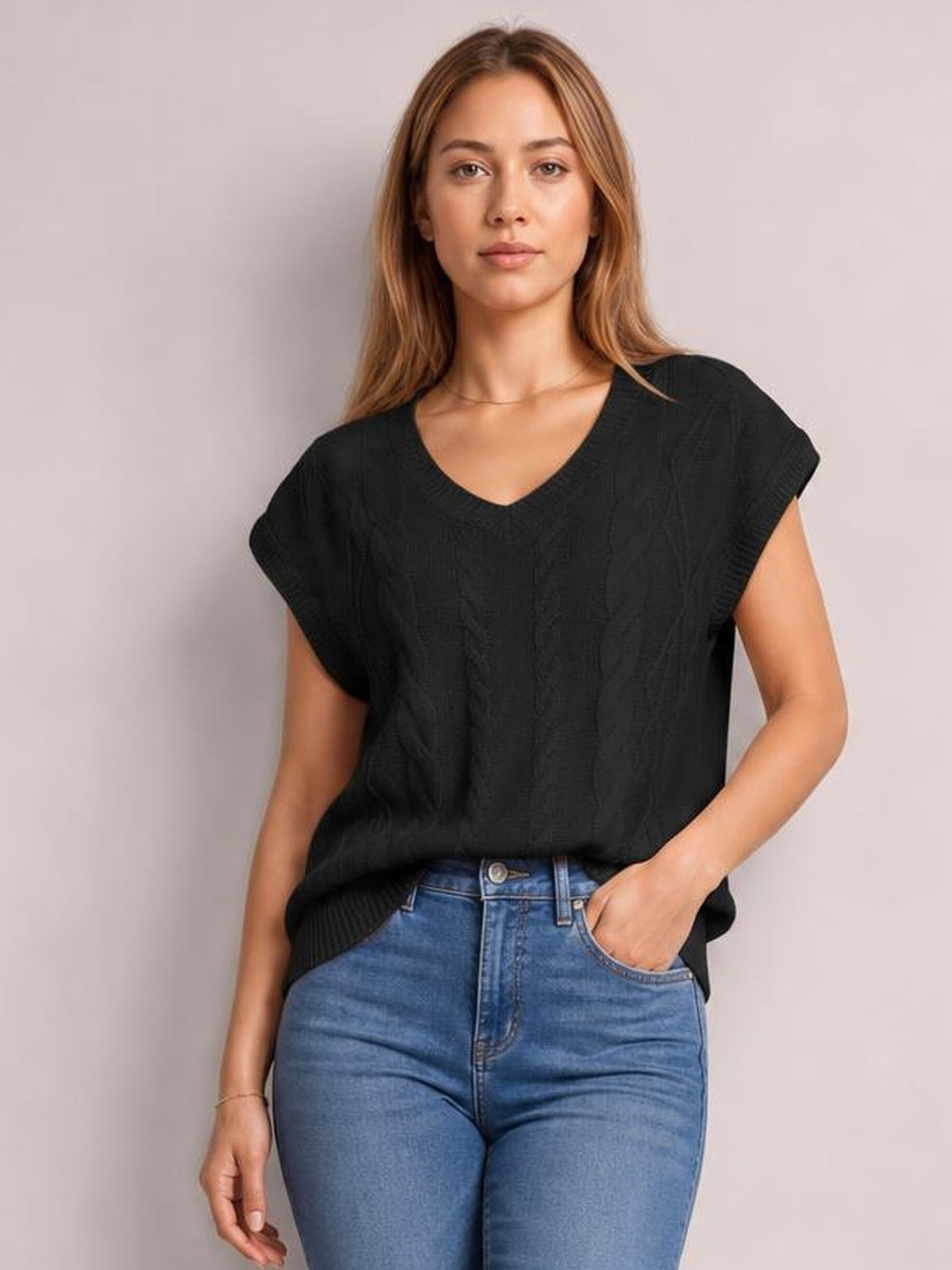 Model wearing a black cable-knit V-neck short sleeve top with a relaxed silhouette and ribbed hem, posing with one hand in her jeans pocket.