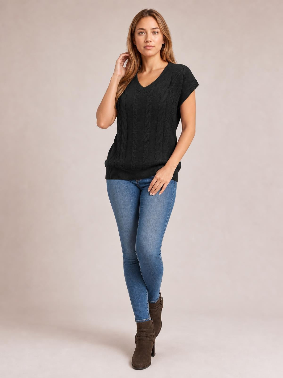 Model poses in a black cable-knit V-neck short sleeve top with a relaxed silhouette, ribbed hem and cuffs, paired with jeans.