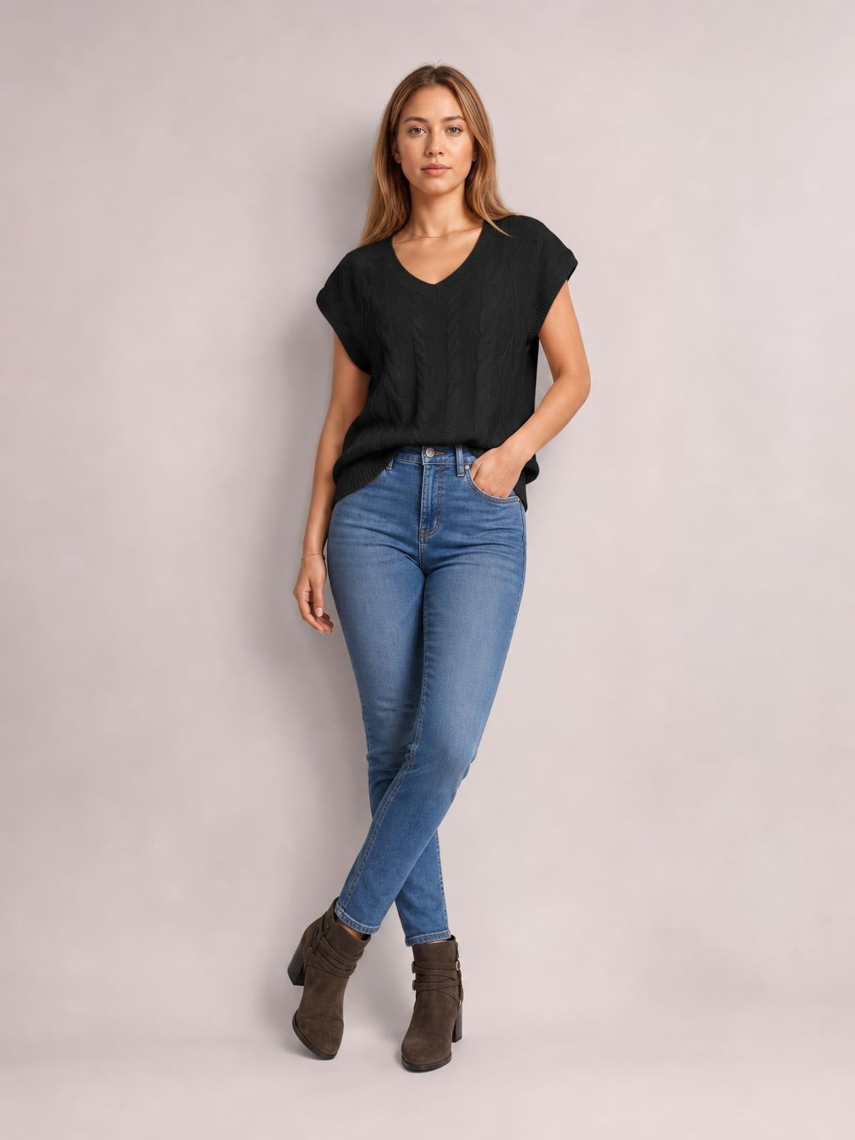 Model wearing a black cable-knit V-neck short sleeve knit top with a relaxed silhouette, ribbed edges, and one hand in her jeans pocket.