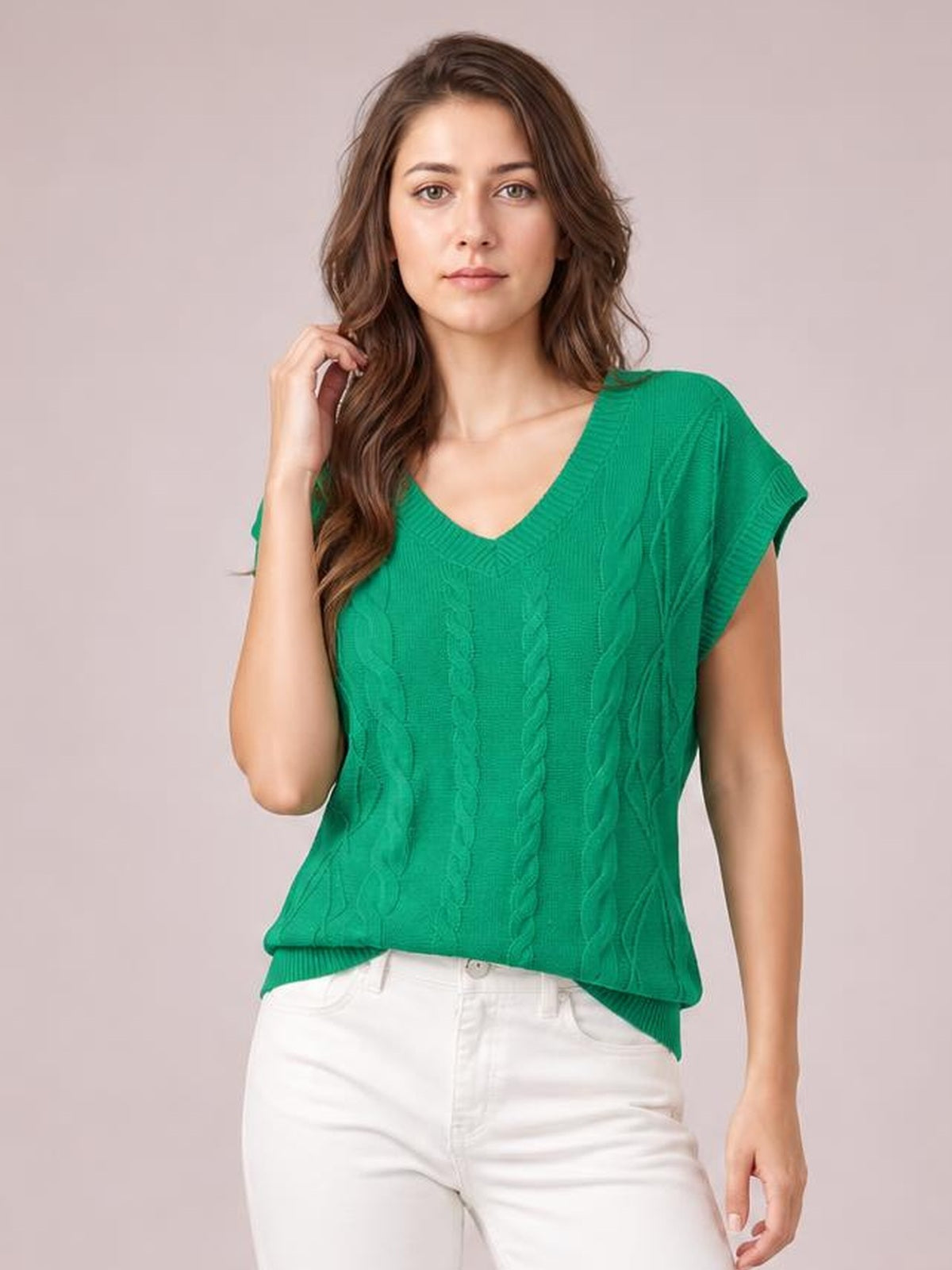 Model wearing a green cable-knit V-neck short sleeve knit top with a relaxed silhouette and ribbed hem, posing with one hand touching her hair.
