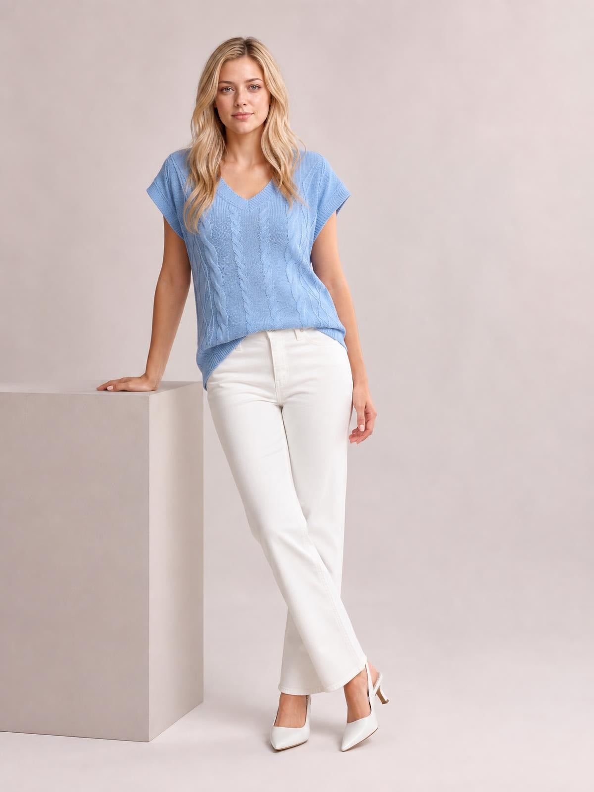 A model leans with one hand on a pedestal while wearing a light blue cable-knit V-neck short-sleeve top with a relaxed, fitted silhouette.
