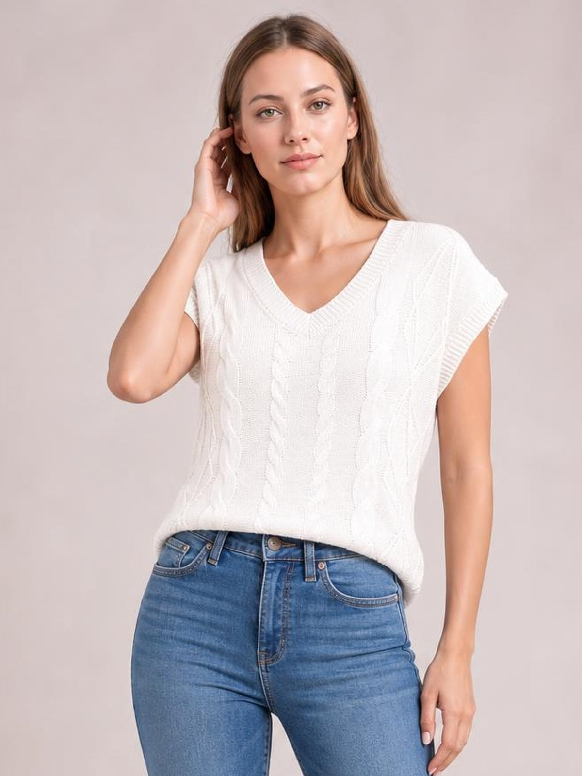 Model wearing a white cable-knit V-neck short sleeve top with a relaxed straight silhouette, ribbed neckline and cuffs, paired with blue jeans while touching her hair.