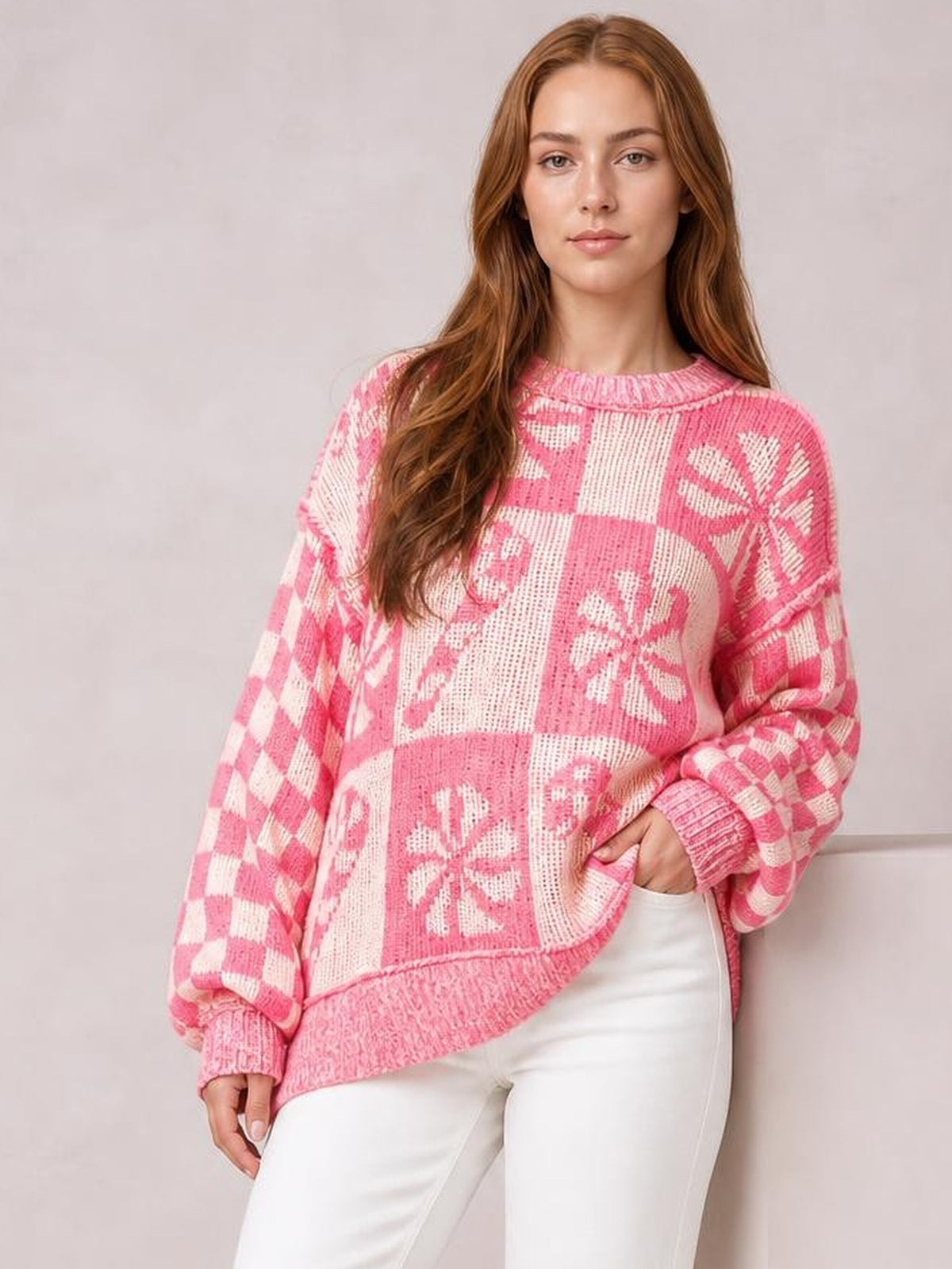 Model wears a pink and white round neck long sleeve sweater with a relaxed silhouette, patchwork floral and checkerboard knit, ribbed cuffs and hem.