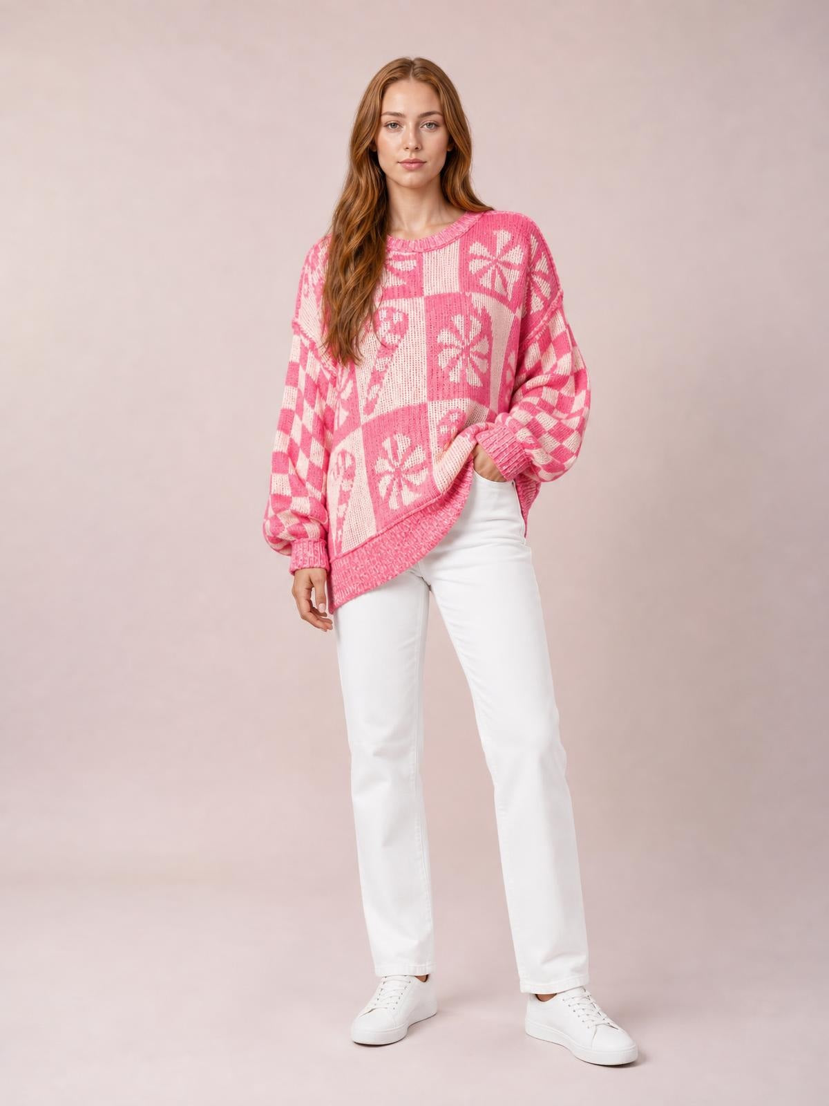 A model poses in a pink and white patterned round neck long sleeve sweater with a relaxed silhouette, ribbed trim, and one hand at her hip.