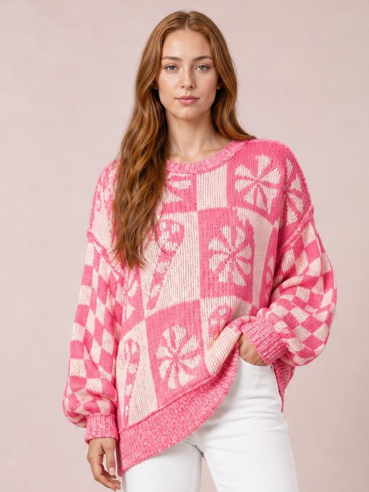 A model poses in a relaxed pink and white round-neck long-sleeve sweater with floral patchwork, ribbed cuffs and hem, and a loose silhouette.