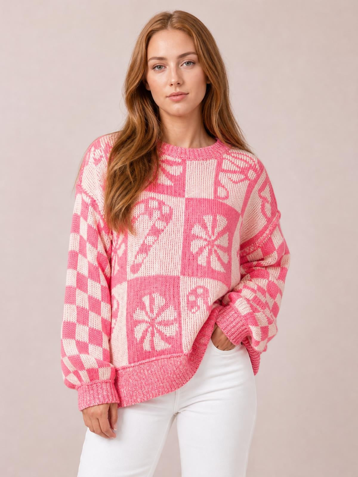 Model wears a pink and white round neck long sleeve sweater with a relaxed silhouette, bold geometric knit pattern, and ribbed cuffs and hem.
