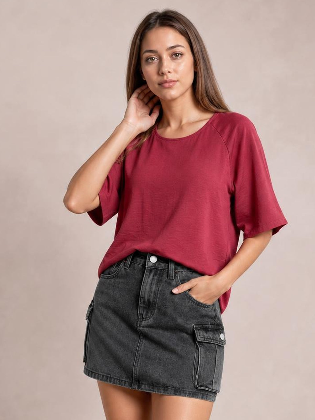 A model poses in a charcoal denim cargo skirt with a straight mini silhouette, belt loops, front pockets, and flap cargo pockets with button closures.