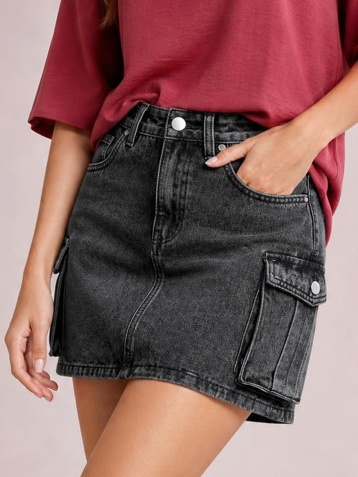 Model wearing a black denim cargo skirt with a high waist, straight mini silhouette, belt loops, front pockets, and flap cargo pockets.
