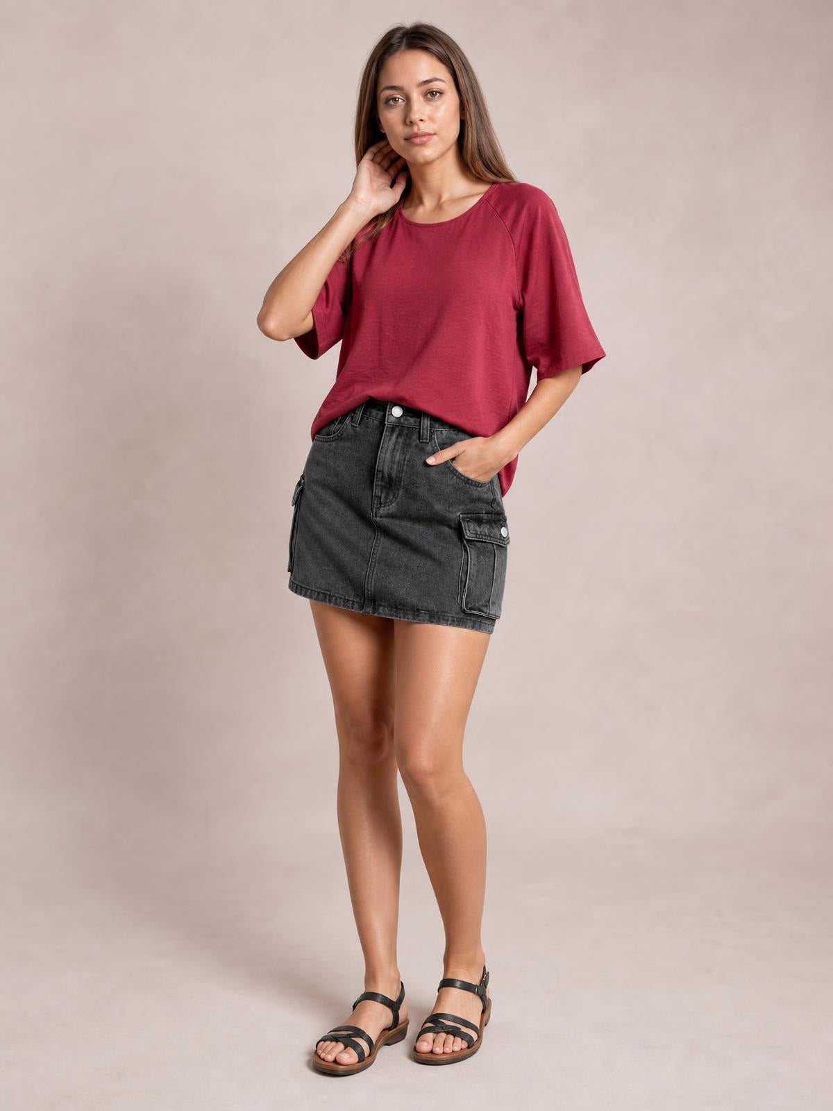 Model poses in a dark charcoal cargo denim skirt with a straight mini silhouette, belt loops, front pockets, and flap cargo pockets with button closures.
